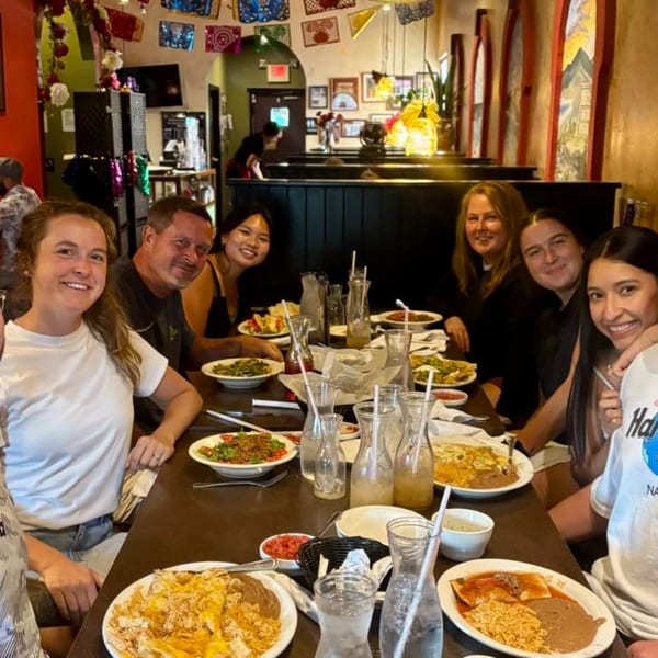 Group of eight smiling people dining at a long table filled with Mexican food and drinks.